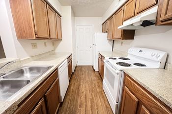 An empty kitchen with wood flooring and white appliances